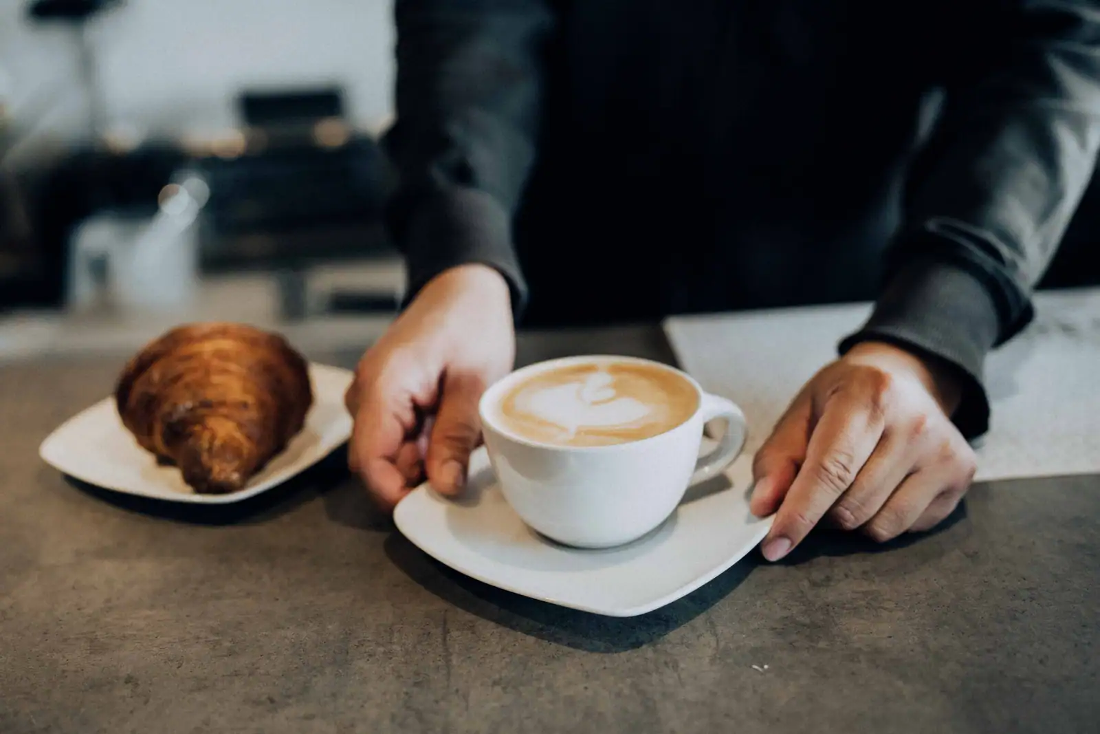 Un serveur pose un cappuccino et une viennoiserie sur le comptoir d'un bar, au moment du petit-déjeuner.