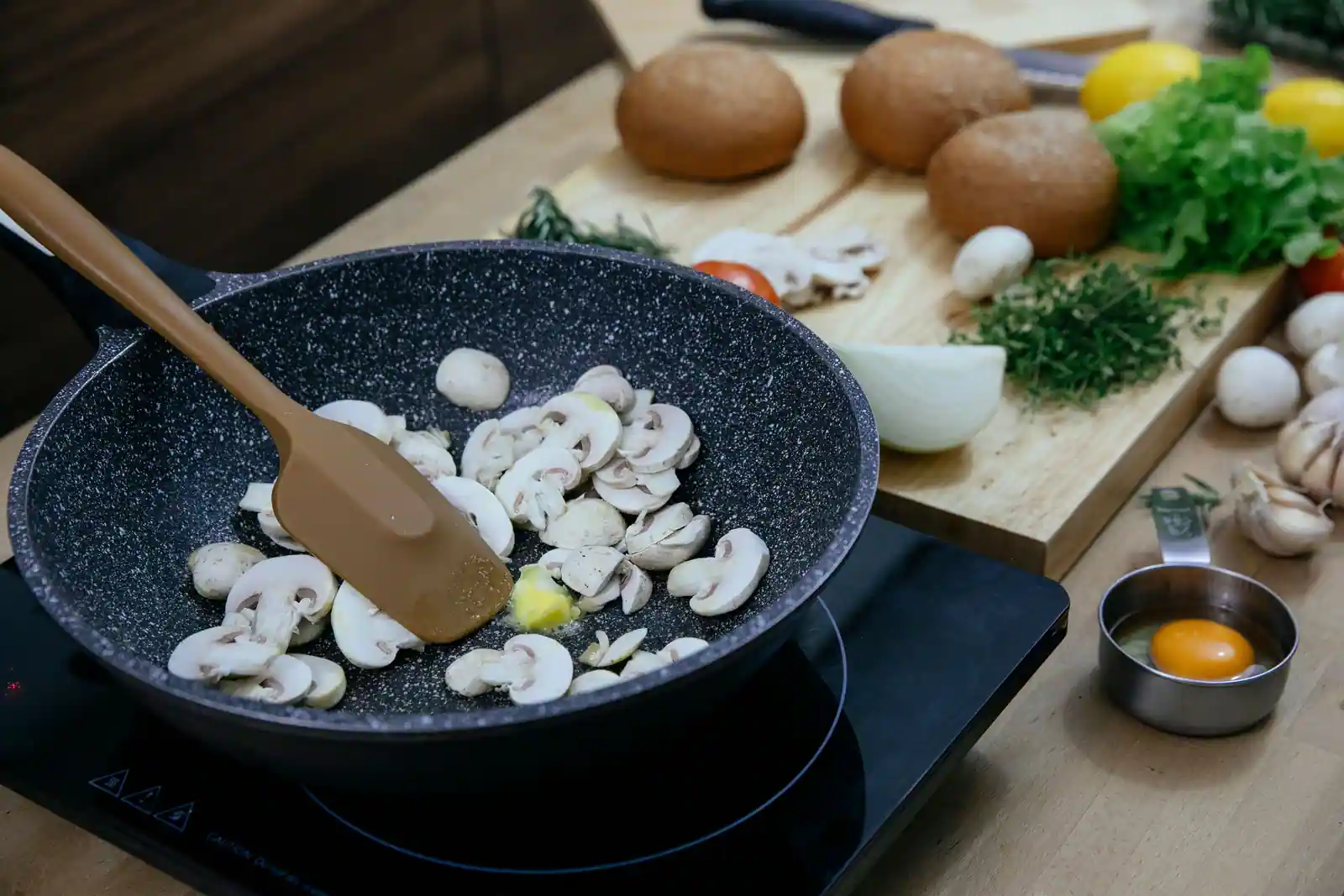Champignons émincés dans une poêle posée sur une plaque, planche de légumes taillés à côté.