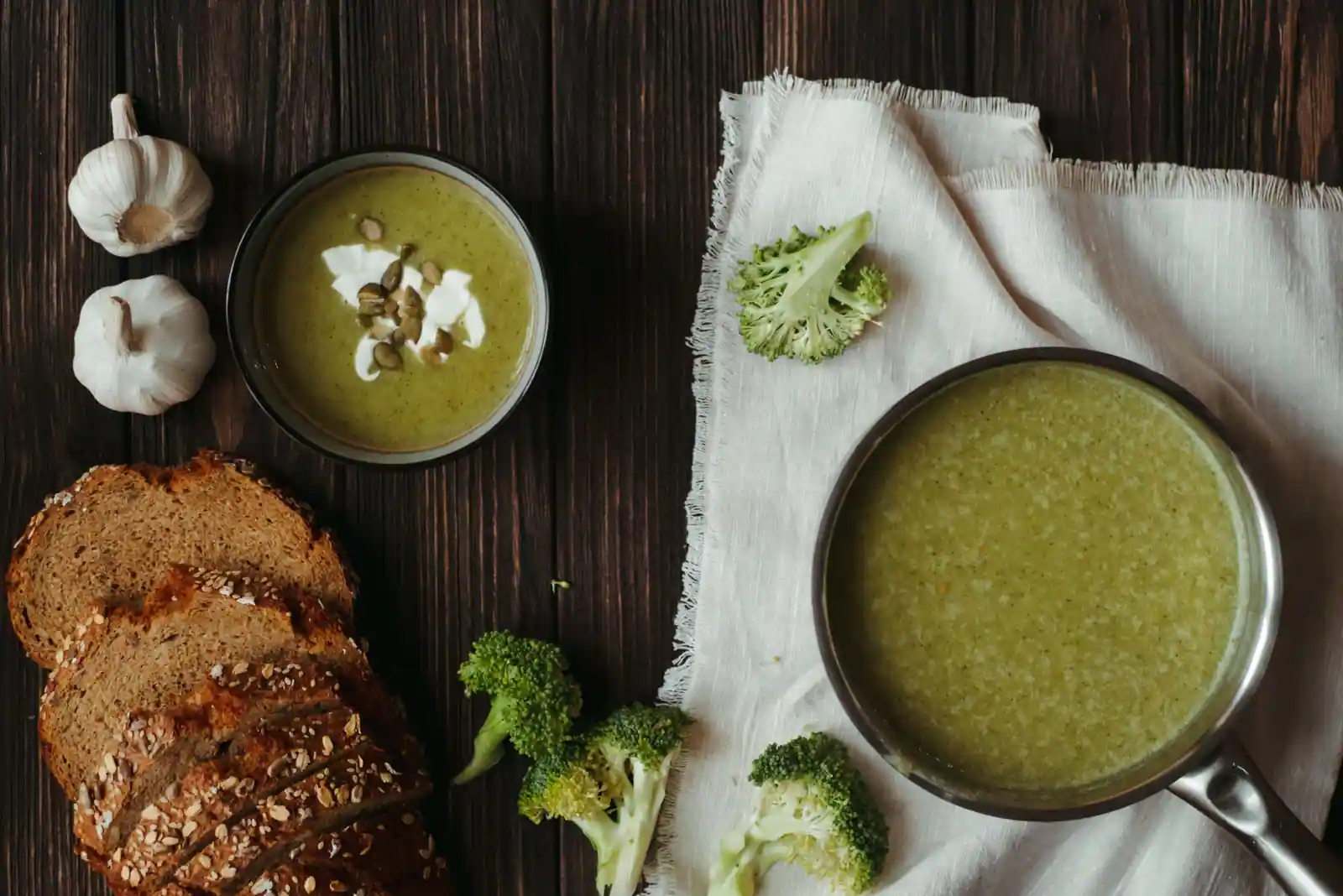 Velouté vert en bol et en casserole, tranches de pain complet et brocolis sur une table en bois