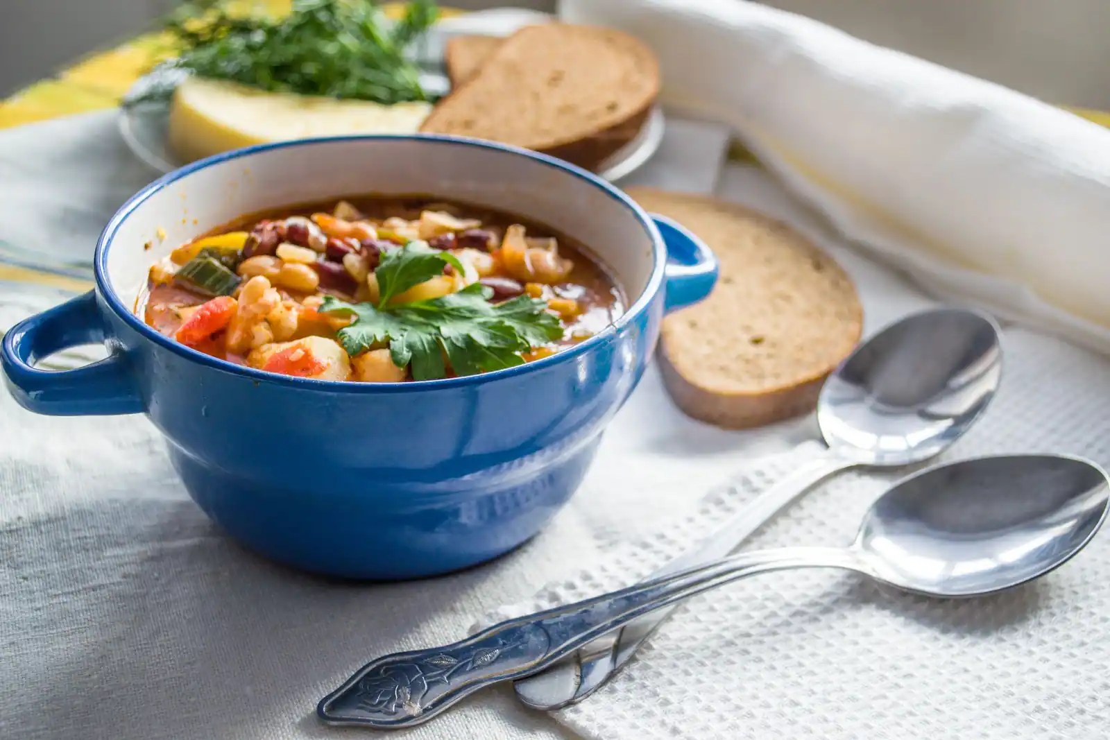 Bol bleu de soupe épaisse aux haricots et légumes, garnie de persil, avec deux tranches de pain complet.