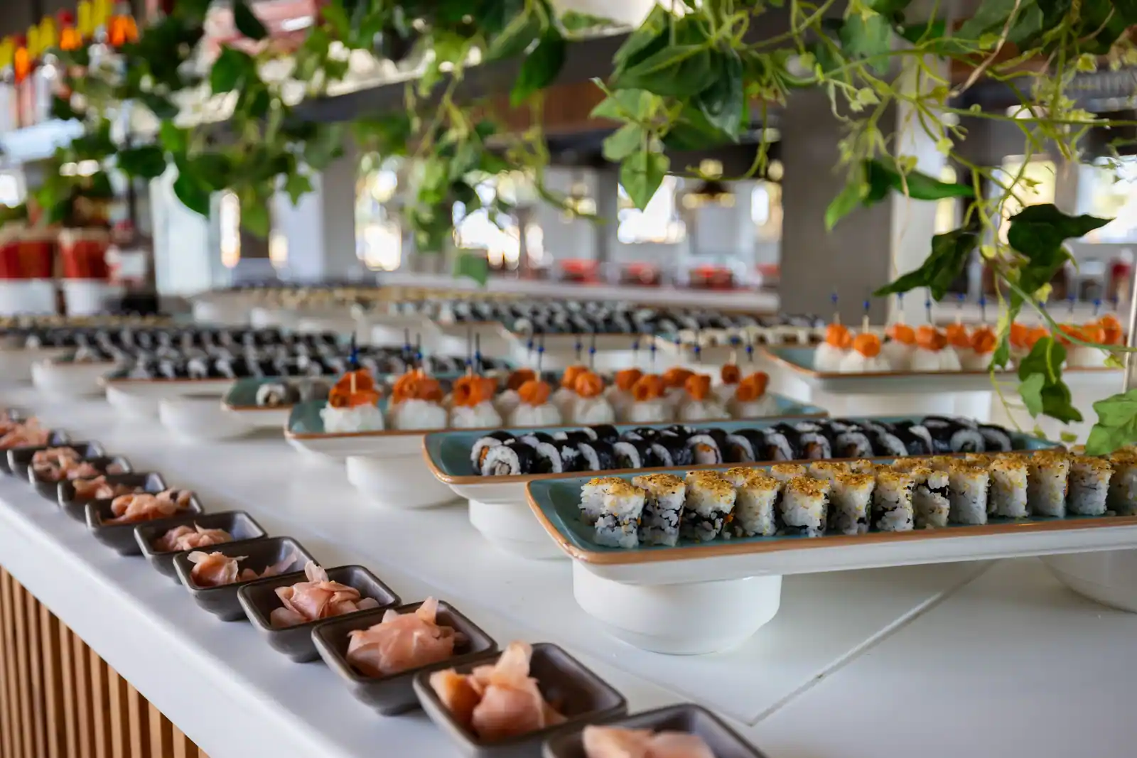 Comptoir de bar à sushis garni de plateaux de makis et de nigiris, avec des coupelles de gingembre.