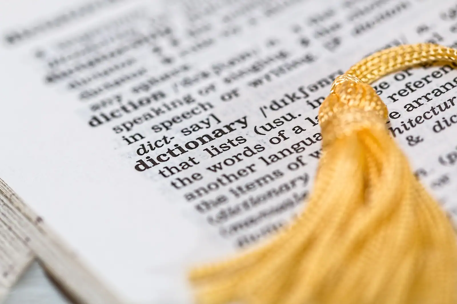 Page de dictionnaire ouverte sur l'entrée du mot dictionary, avec un signet à pompon doré posé dessus.