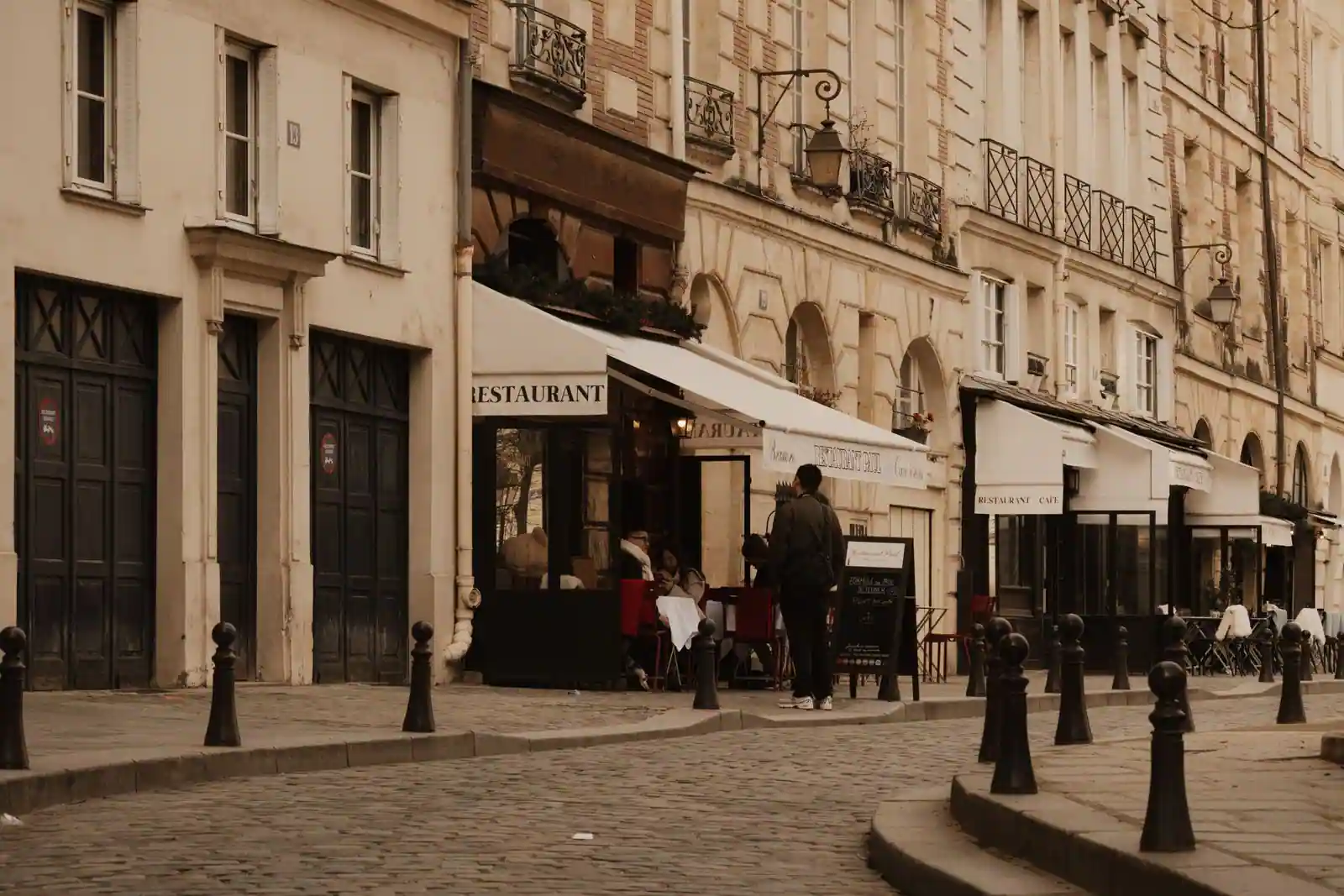 Terrasse de café en bord de rue pavée, façades haussmanniennes typiques d'un quartier parisien