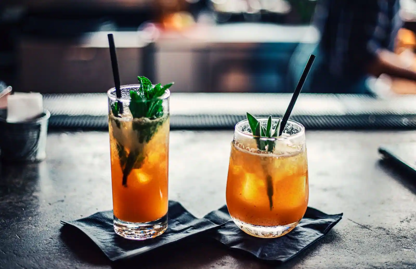 Deux cocktails ambrés garnis de menthe fraîche, servis dans des verres sur un comptoir de bar