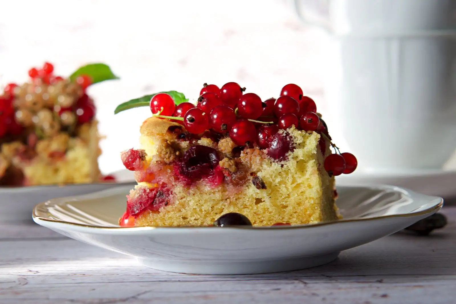Part de gâteau moelleux tranchée, mie dorée et régulière, posée sur une assiette avec un fouet et un bol de farine en arrière-plan