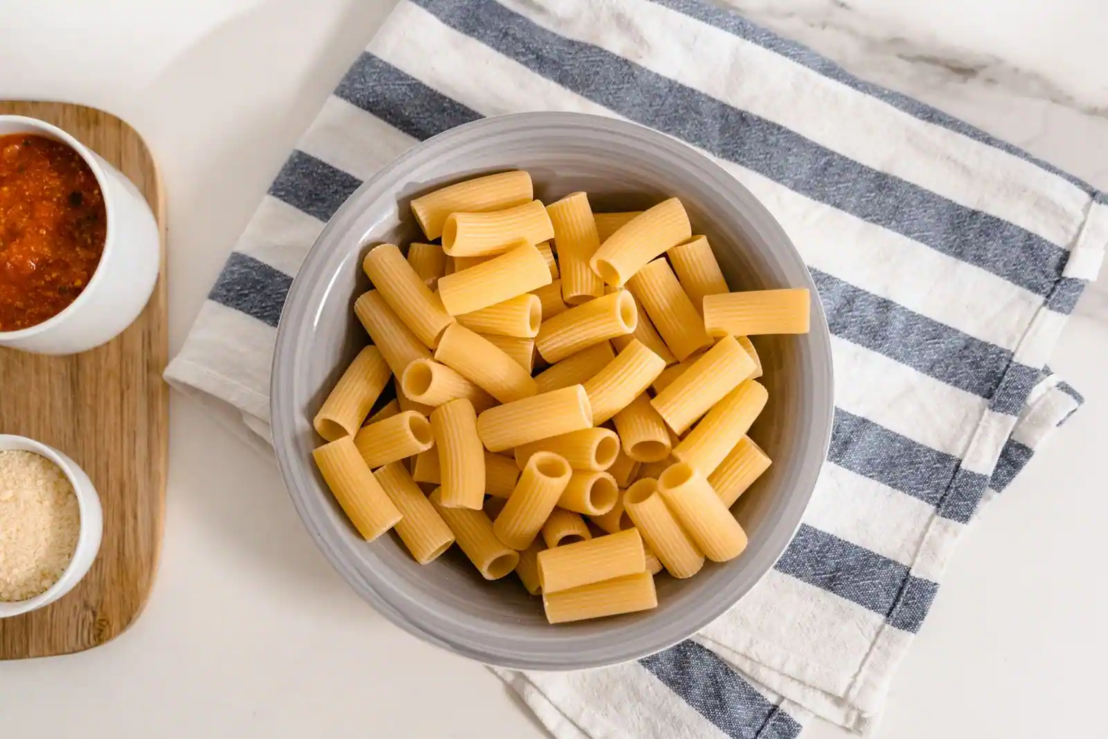 Bol de pâtes courtes striées nappées de sauce tomate, parsemées de parmesan râpé, en gros plan.