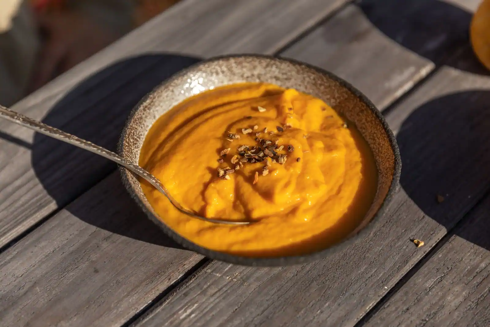 Velouté de potimarron orange servi dans une petite tasse sur une table en bois