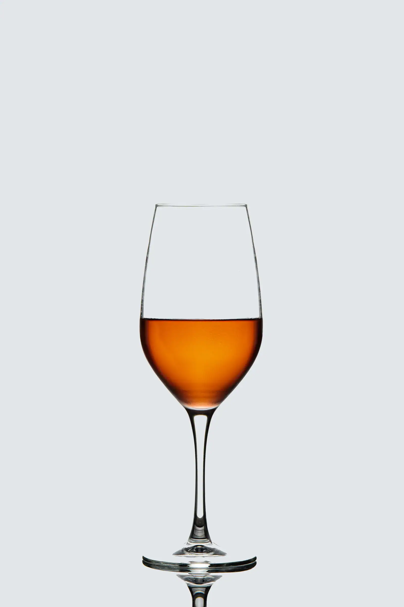 Verre de vin orange à la robe ambrée sur fond neutre, couleur cuivrée typique de la macération des peaux